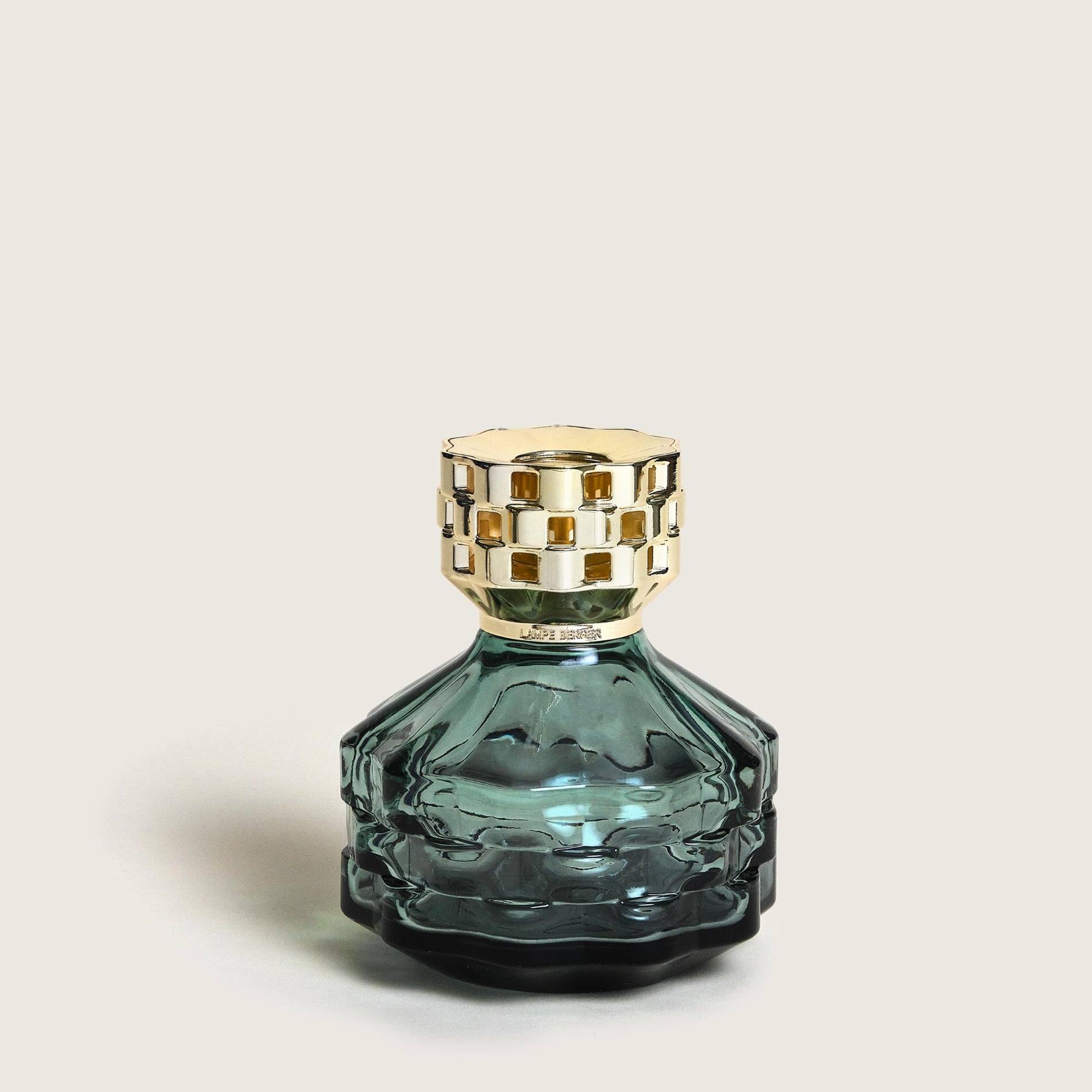 Green/black glass fragrance diffuser with gold top on a light beige background