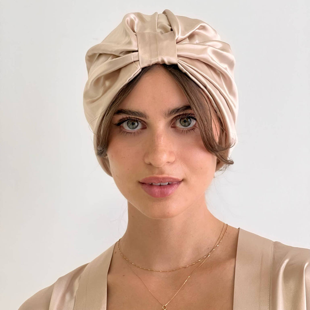 Woman wearing a beige satin turban against a plain background