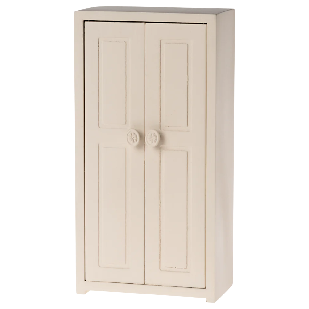 A small toy closet in a cream color with two doors and three golden hangers inside.