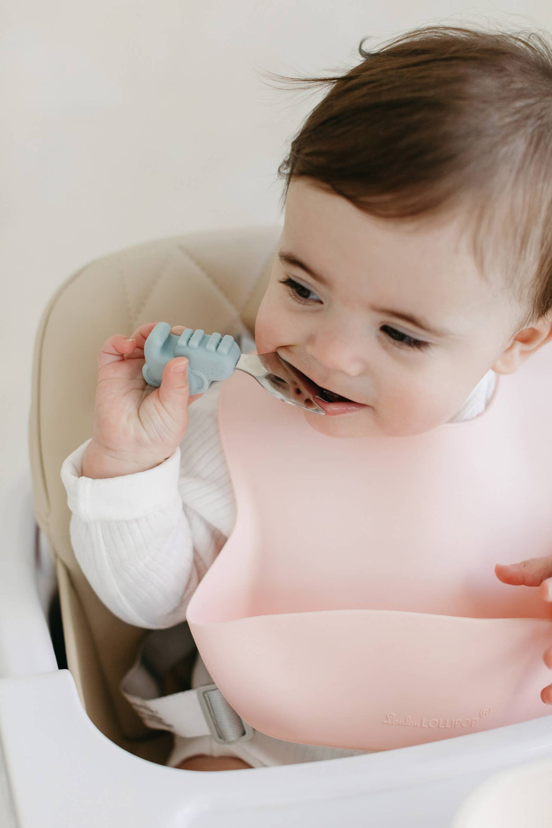 Baby sitting in a high chair holding a blue object, smiling.
