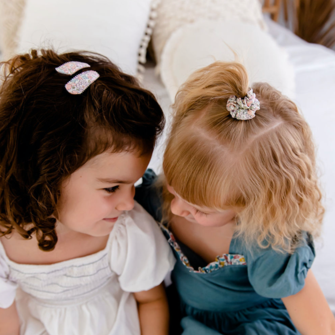 Two young girls sitting close together, wearing decorative hair clips.