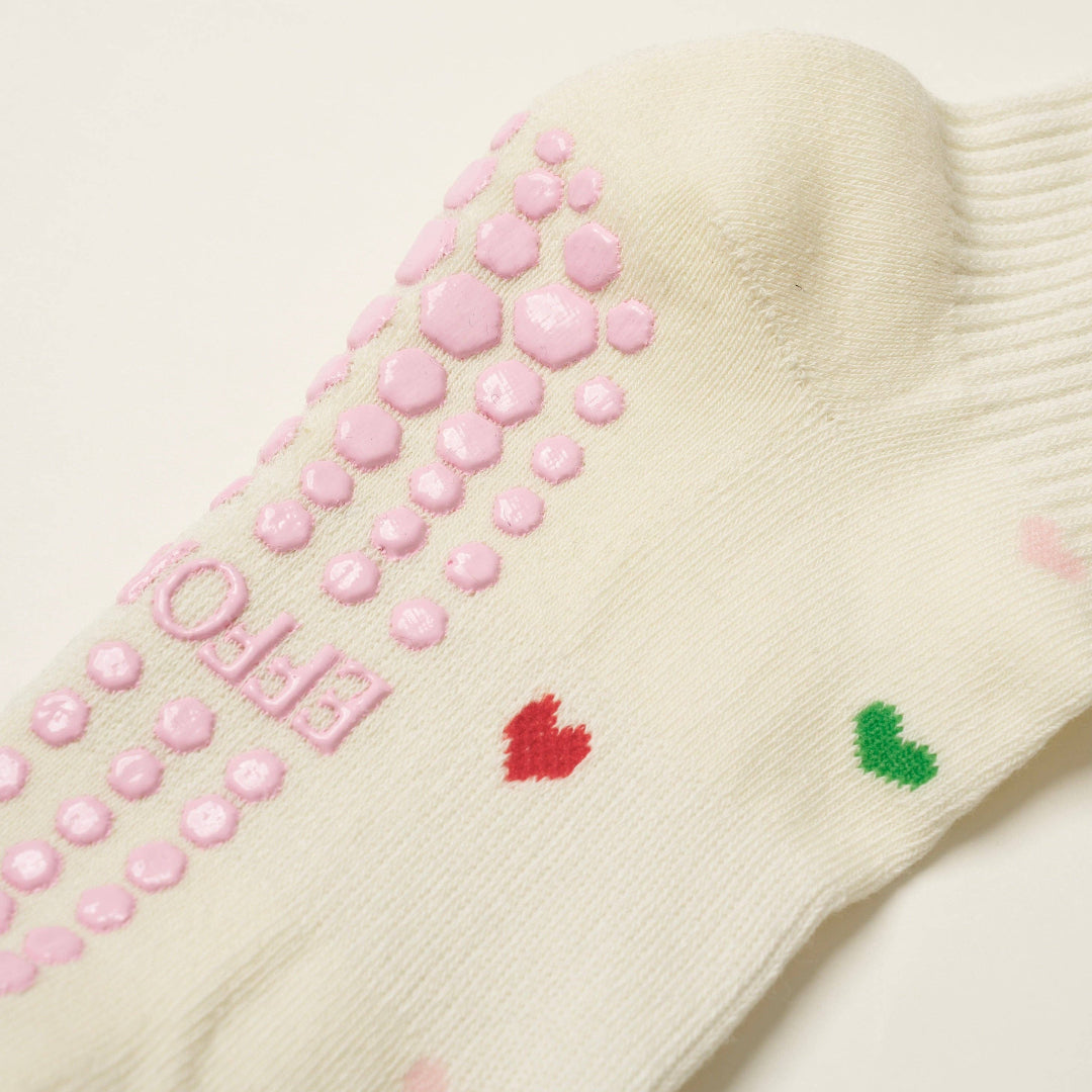 Beige sock with pink grip dots and colorful hearts on a light background