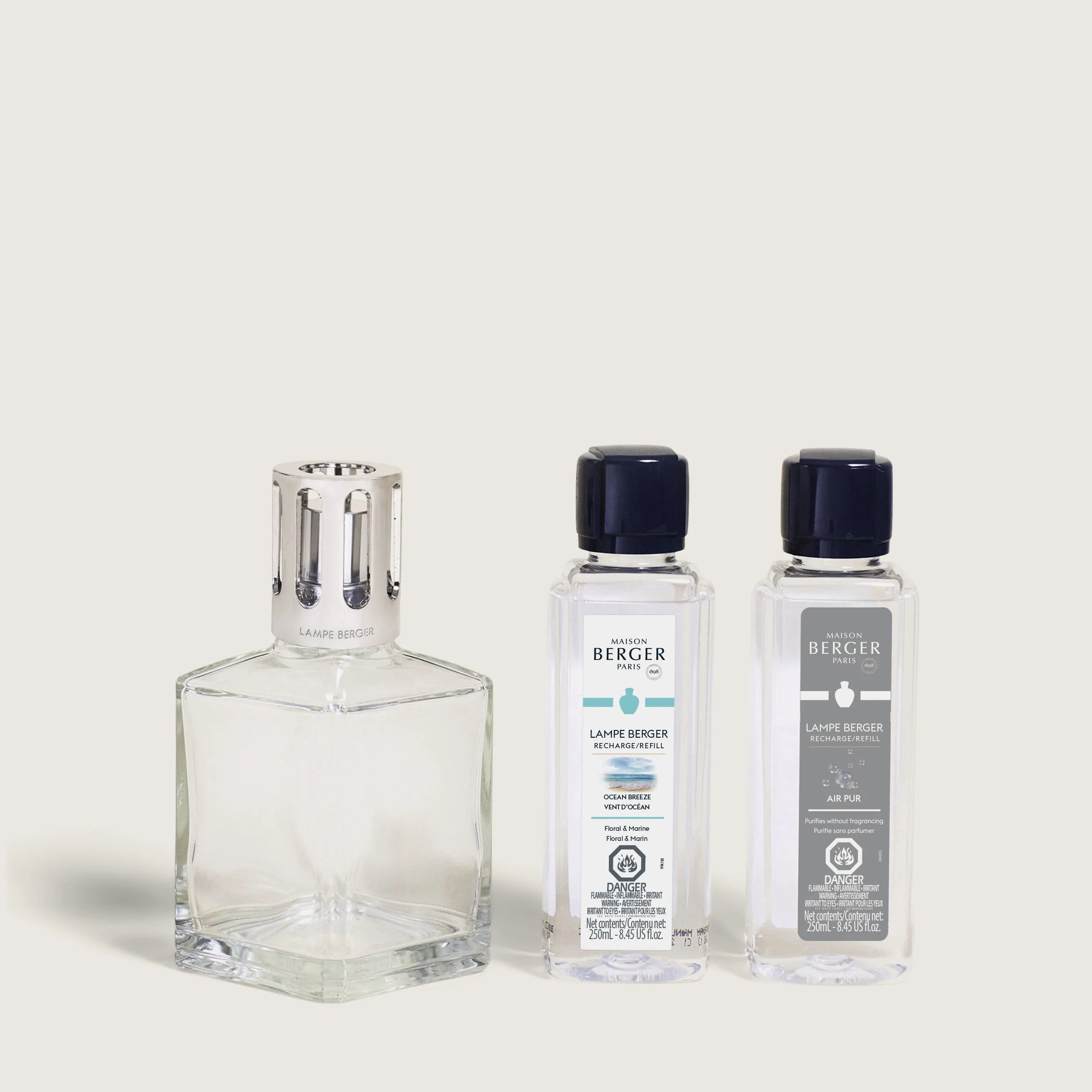 A Maison Berger fragrance lamp with a square glass base and metal top, accompanied by two bottles of fragrance refills labeled So Neutral and Ocean Breeze.