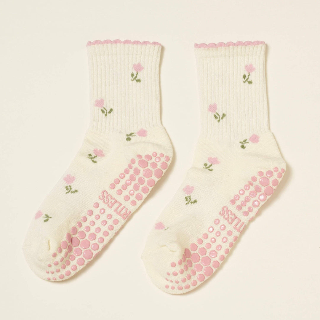 Pair of socks with pink grip dots and floral pattern on a beige background
