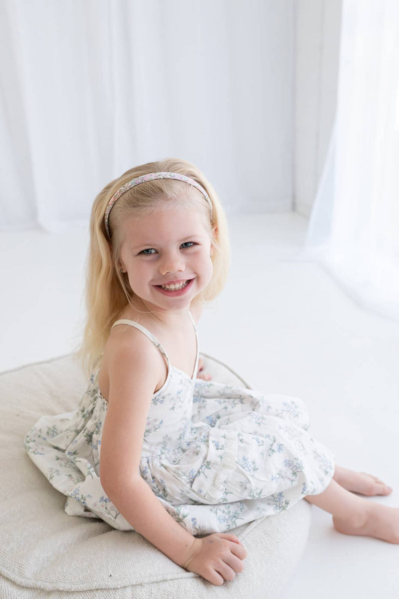 Young girl in a floral dress sitting on a white surface with a white curtain background