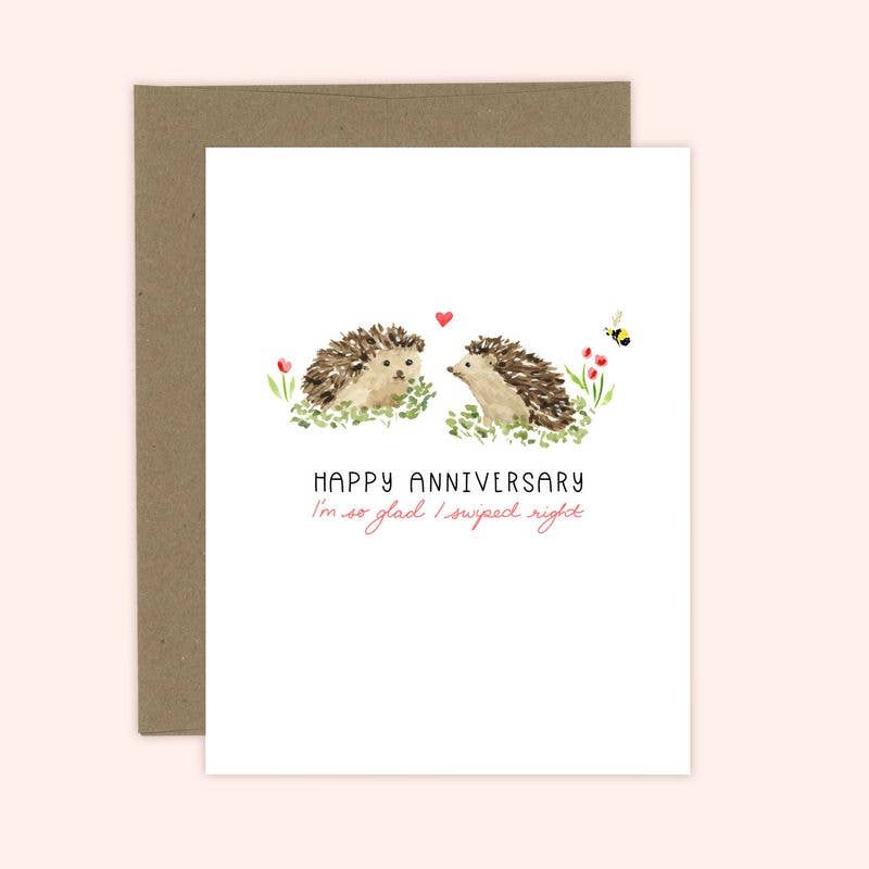 A greeting card with an illustration of two hedgehogs and the text 'Happy Anniversary' on it, accompanied by a brown envelope.
