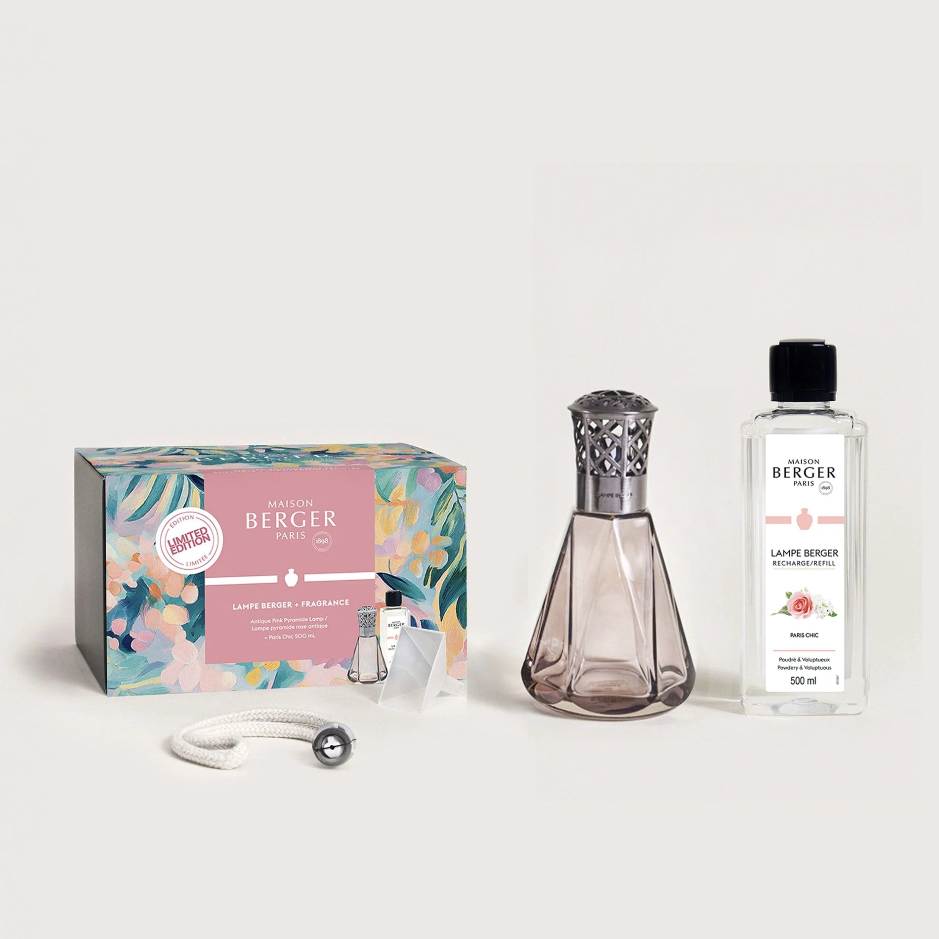 A gift set of a fragrance lamp with an antique pink pyramid design, accompanied by a bottle of rose-forward fragrance and a decorative box with floral patterns.
