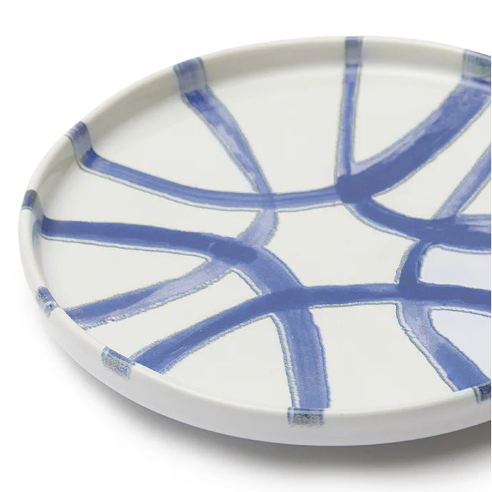 A round white ceramic plate with a blue hand-painted abstract geometric pattern, photographed on a clean white background.
