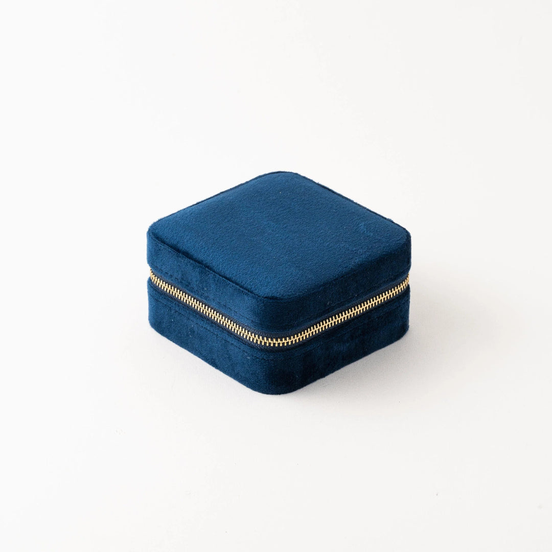 A compact square travel case in blue velvet with a gold coloured zipper.