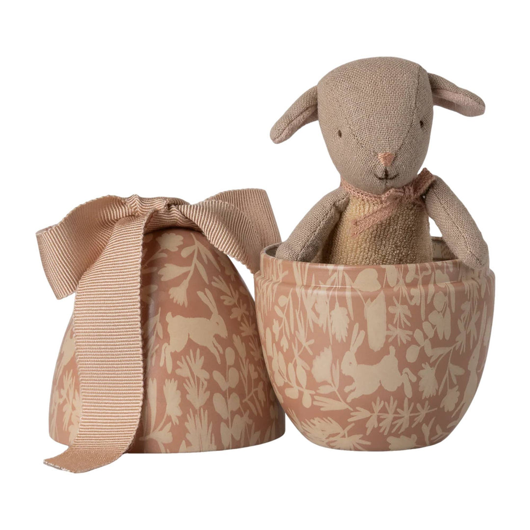 Stuffed lamb toy in a tin egg with a bow on a white background