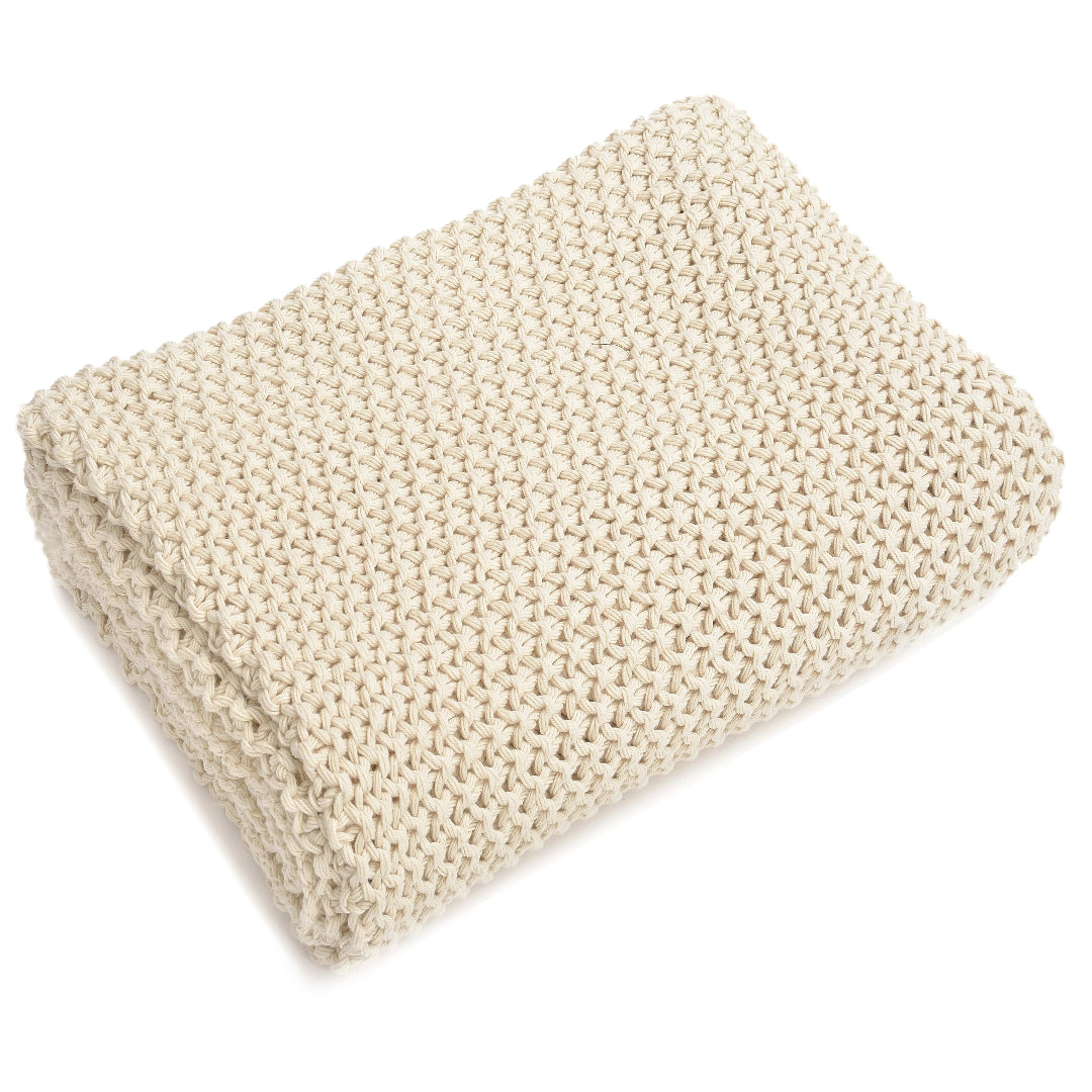 A beige, chunky-knit cotton throw blanket folded at the bottom, displaying its textured pattern.