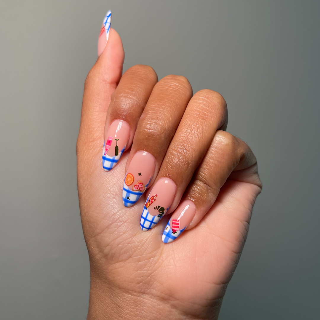 A close-up of a hand displaying long, almond-shaped nails with a French tip design, decorated with blue and white plaid patterns and small colorful nail stickers