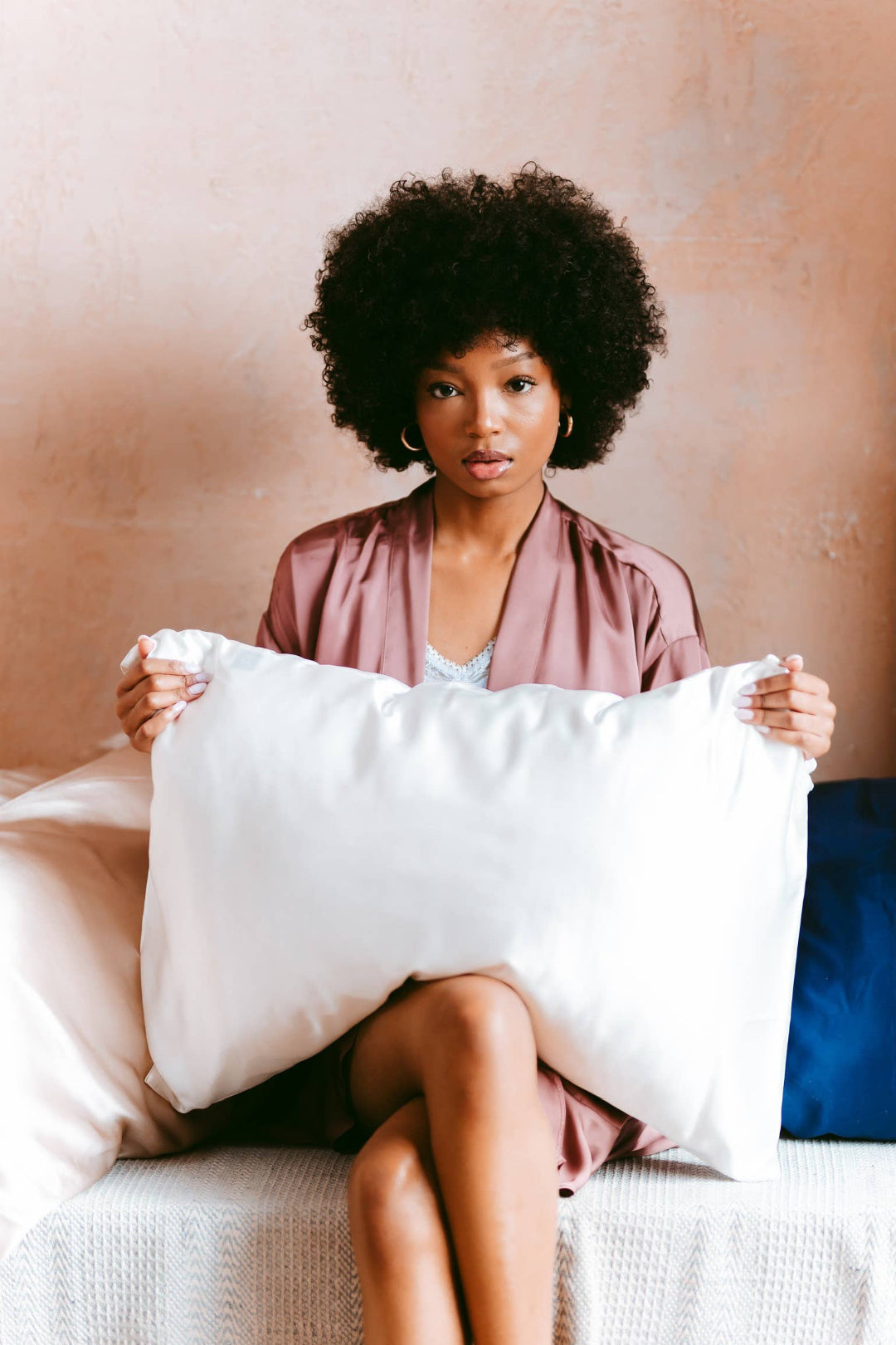 Woman holding a large white pillow against a neutral background