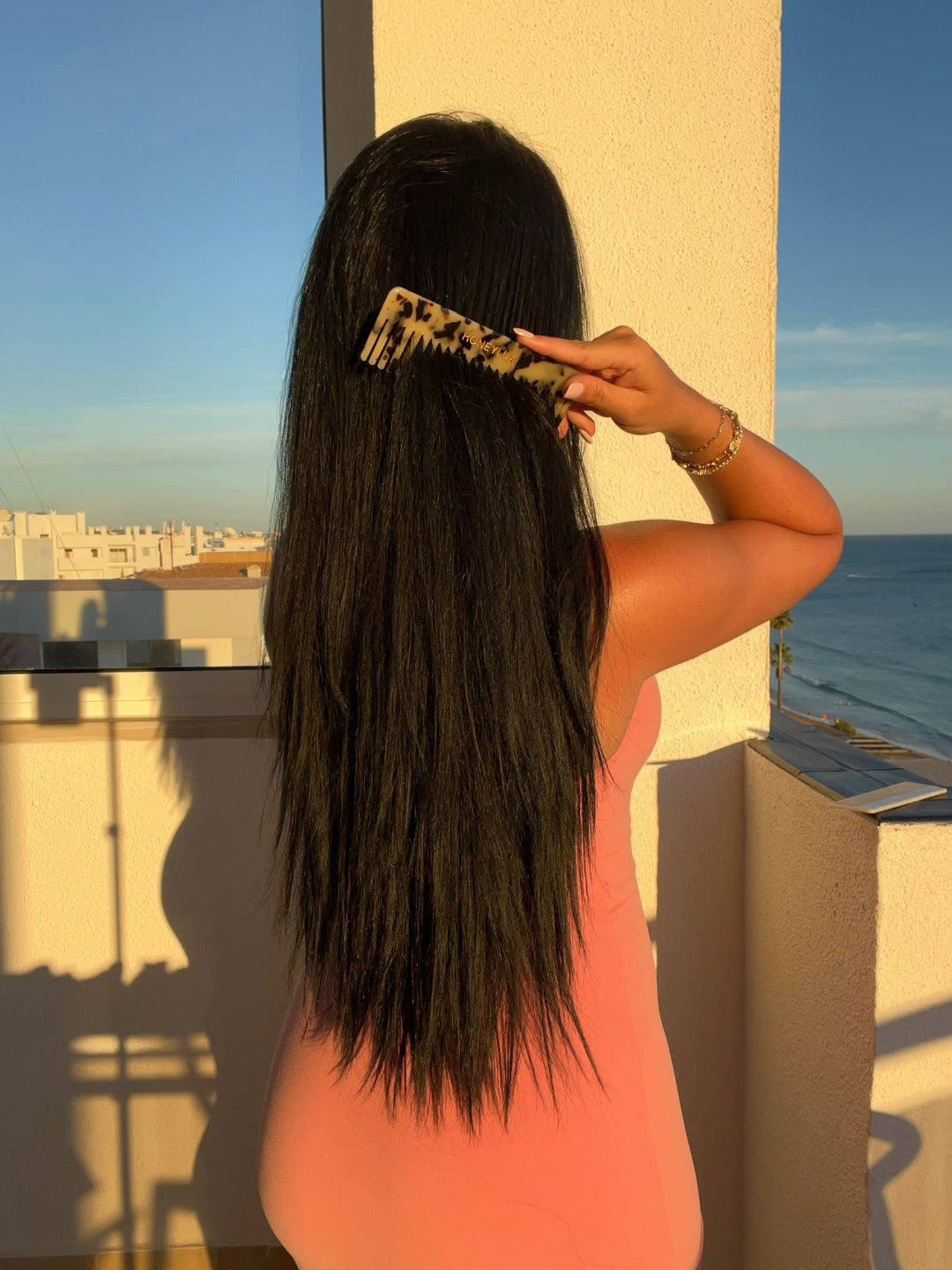 Woman combing her hair on a balcony with a scenic view of the ocean.