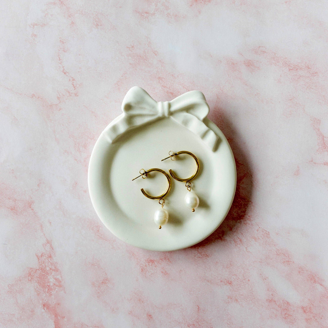 Gold earrings with pearls on a white dish with a bow on a pink marble background