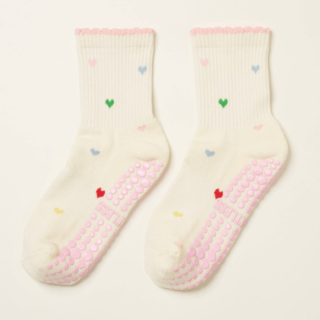 Pair of cream socks with pink textured sole and colorful heart patterns on a beige background
