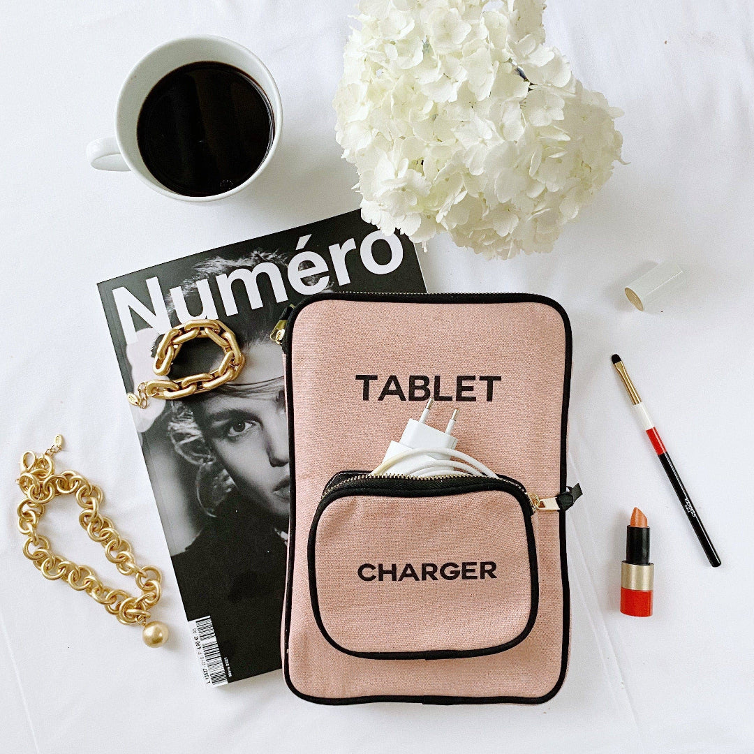 Pink tablet charger case on a white surface with a magazine, coffee, flowers, and makeup items.