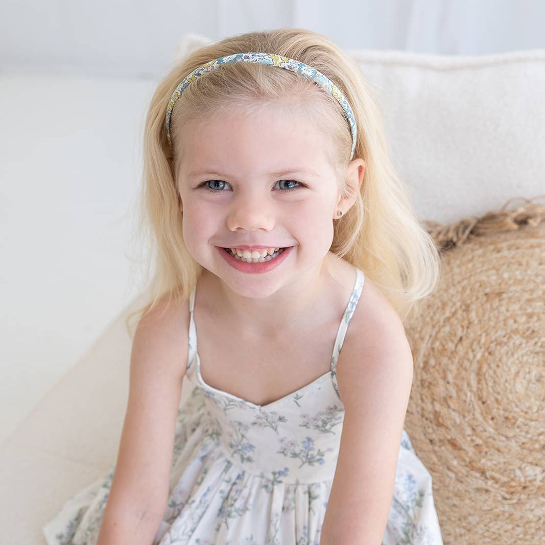 Young girl in a floral dress sitting on a couch with a neutral background