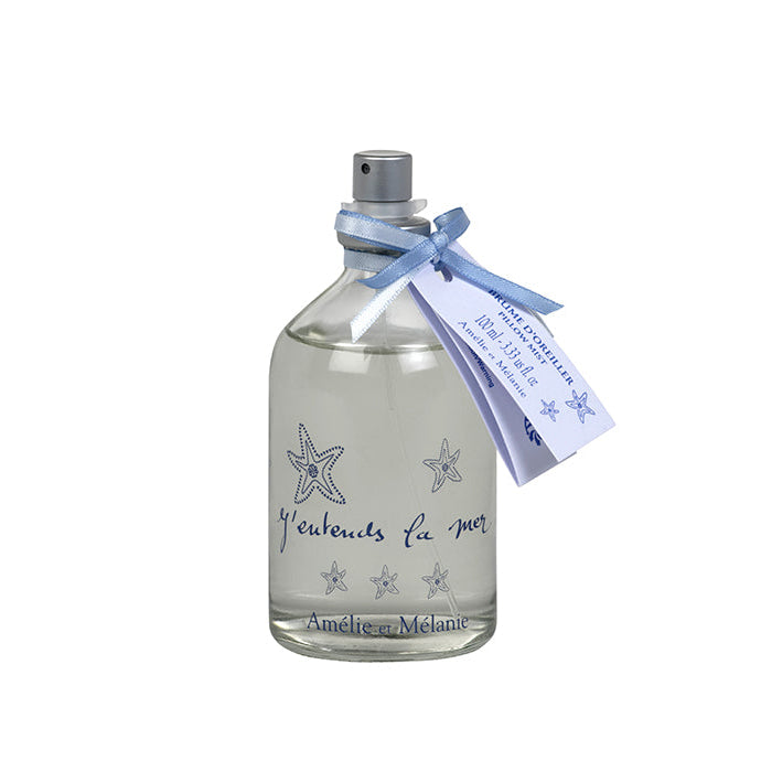 A clear glass bottle with a spray dispenser containing a marine scented pillow mist, adorned with a blue ribbon and labeled 'J'entends la Mer' in a decorative script.