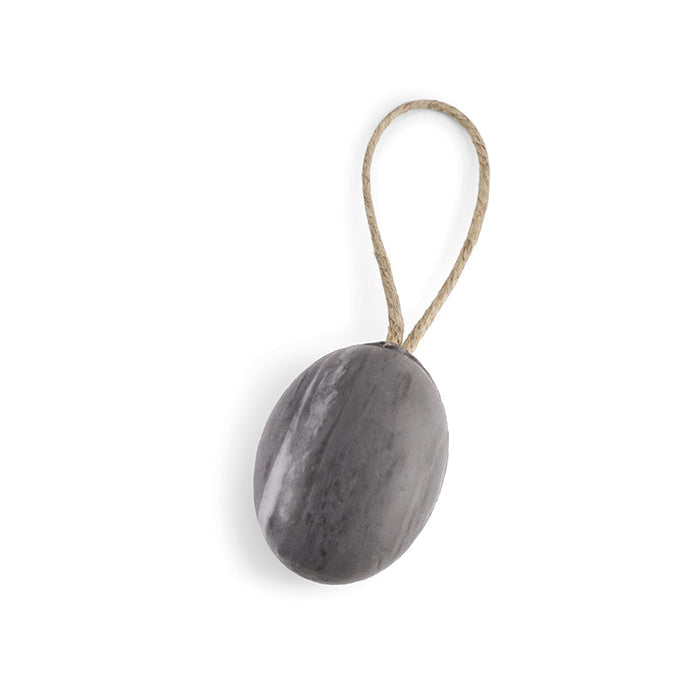 A round piece of gray soap attached to a rope, with a natural and rustic appearance, against a white background.