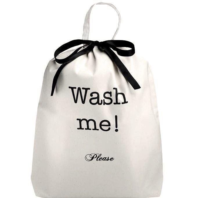 A white laundry bag with the text 'Wash me!' printed on the front, tied with a black ribbon.