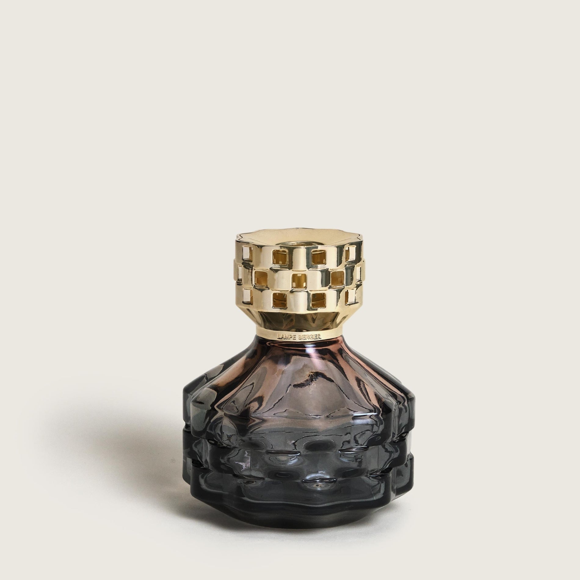 Smoky glass perfume bottle with gold cap on a light beige background
