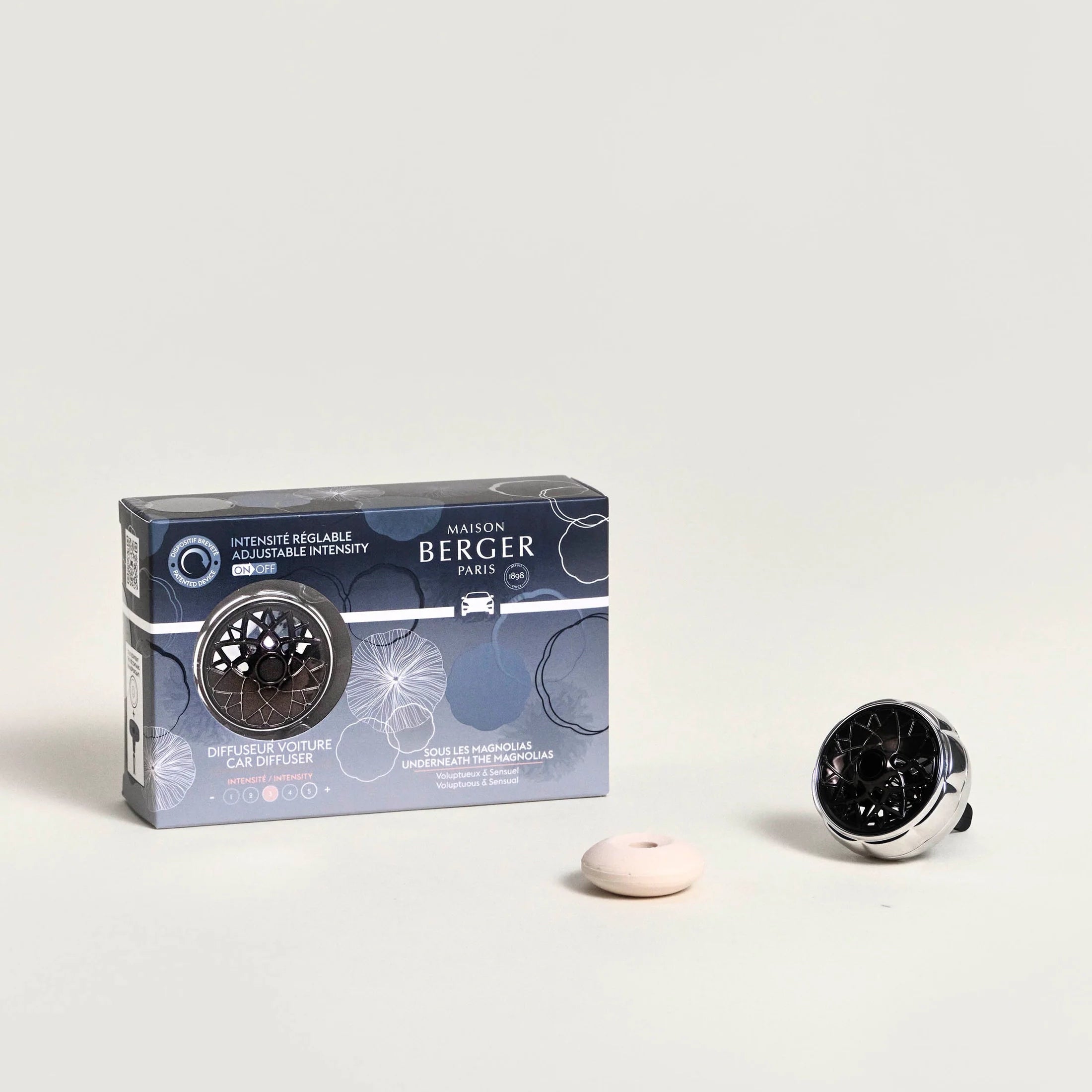 Technical car diffuser kit with underneath the magnolias fragrance, by Maison Berger Paris, displayed with its packaging and a clip-on diffuser.