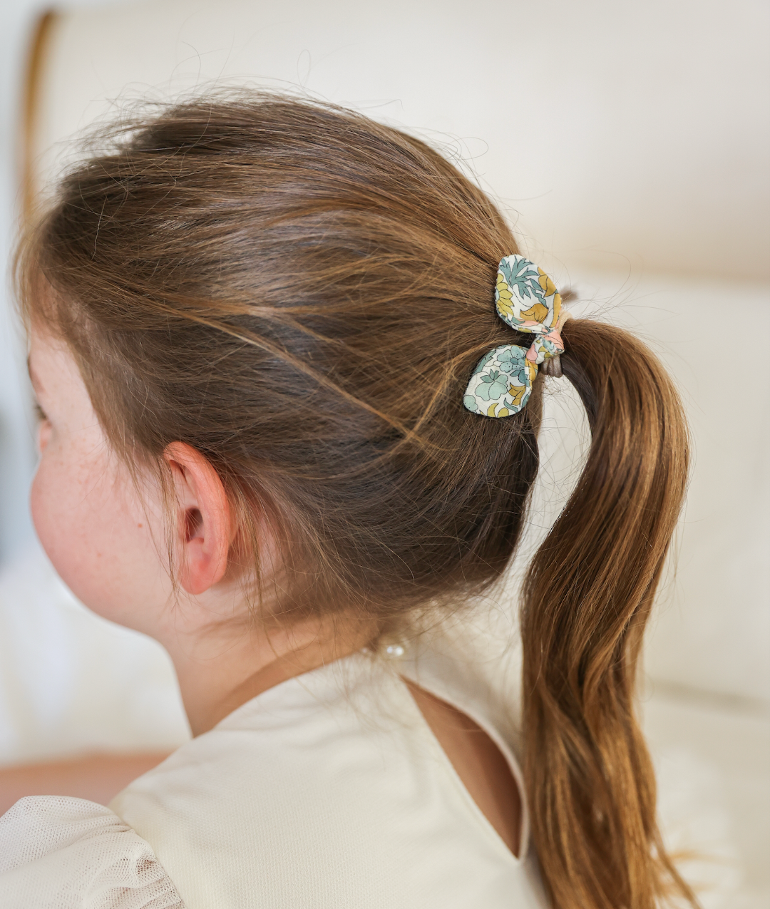 Child with a decorative hair elastic in their hair against a neutral background