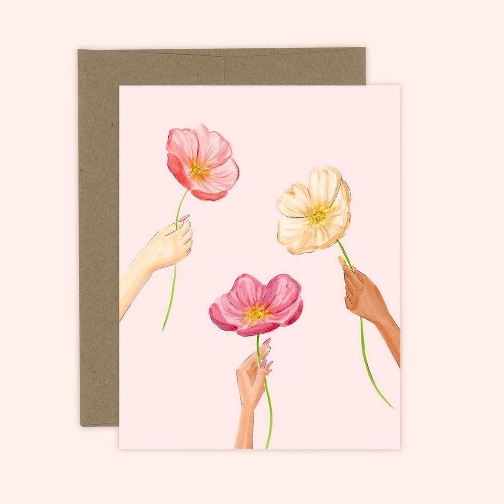 A greeting card with a digital print of pink and white poppies being offered by hands against a white background. The card is accompanied by a brown envelope.