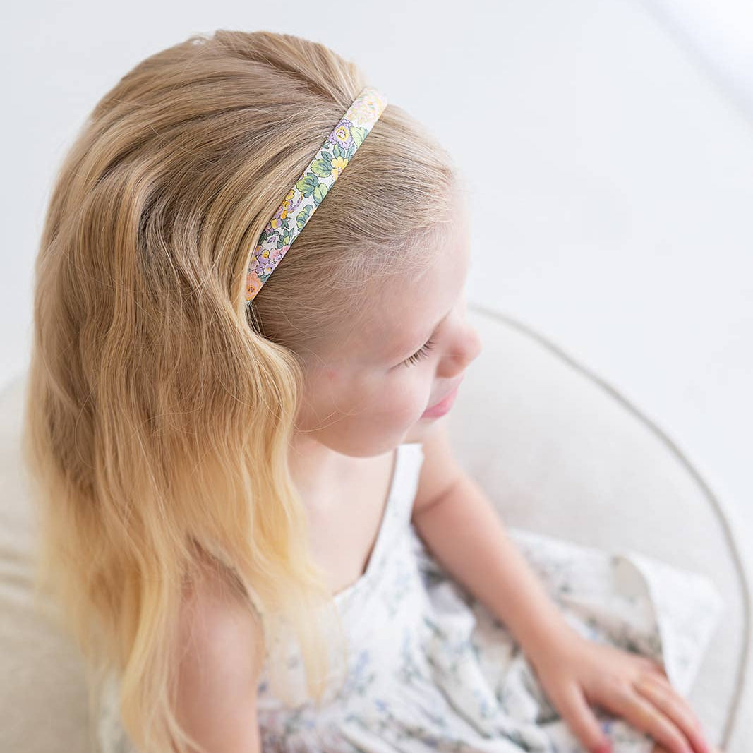 Young girl with blonde hair wearing a decorative headband, sitting on a white surface.