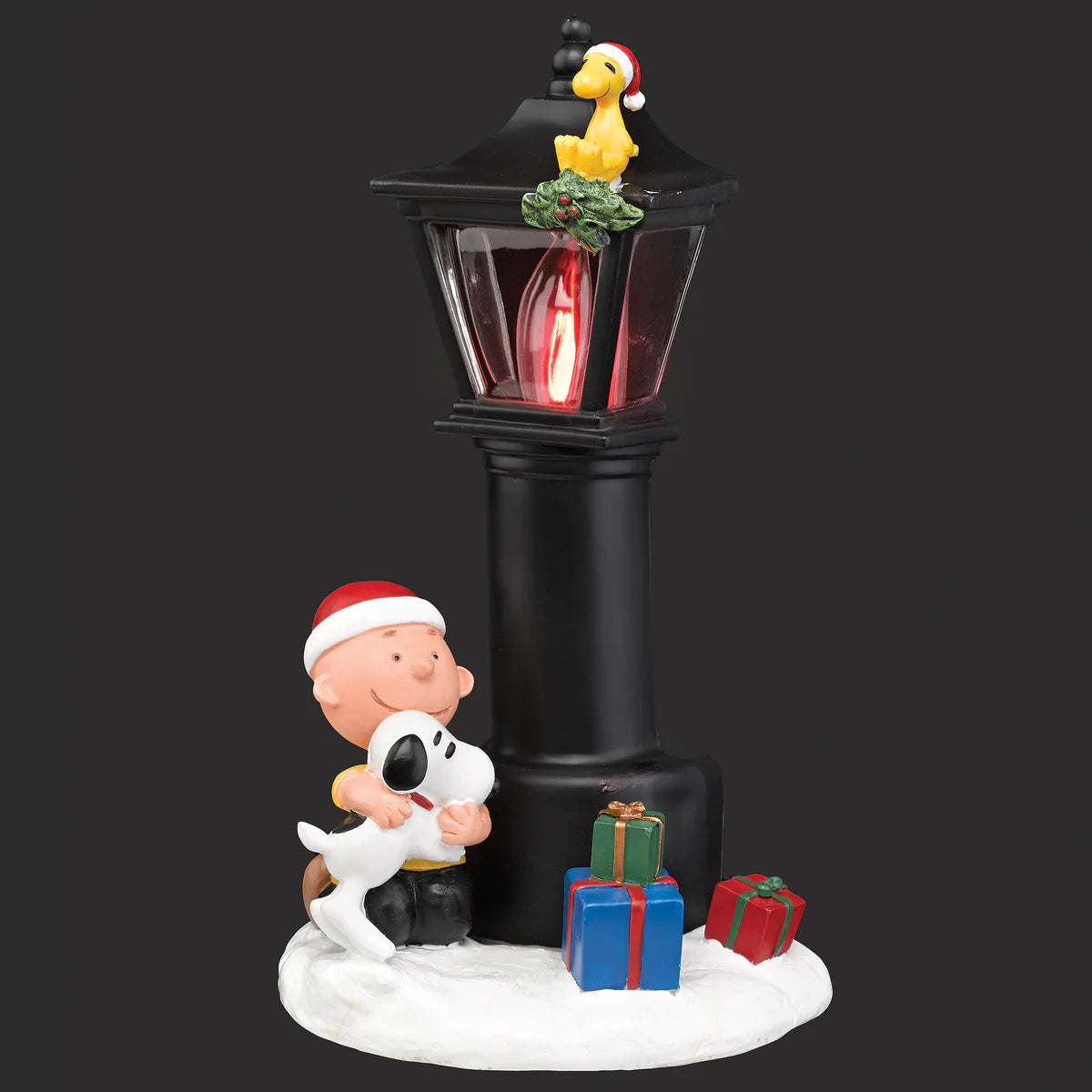 Decorative figurine with Charlie Brown, Snoopy, and a street lamp with presents underneath on a black background.