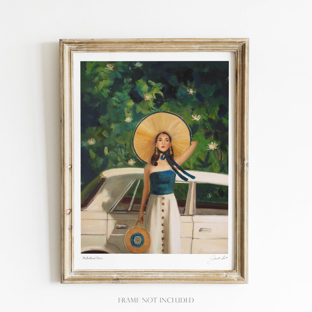 A framed art print featuring a woman with a straw hat and a blue dress, sitting in a car with a tree in the background. The frame is wooden and the artwork is signed by the artist.
