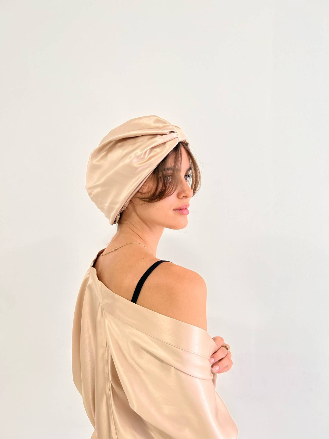 Woman wearing a beige hair wrap and draped fabric against a light background
