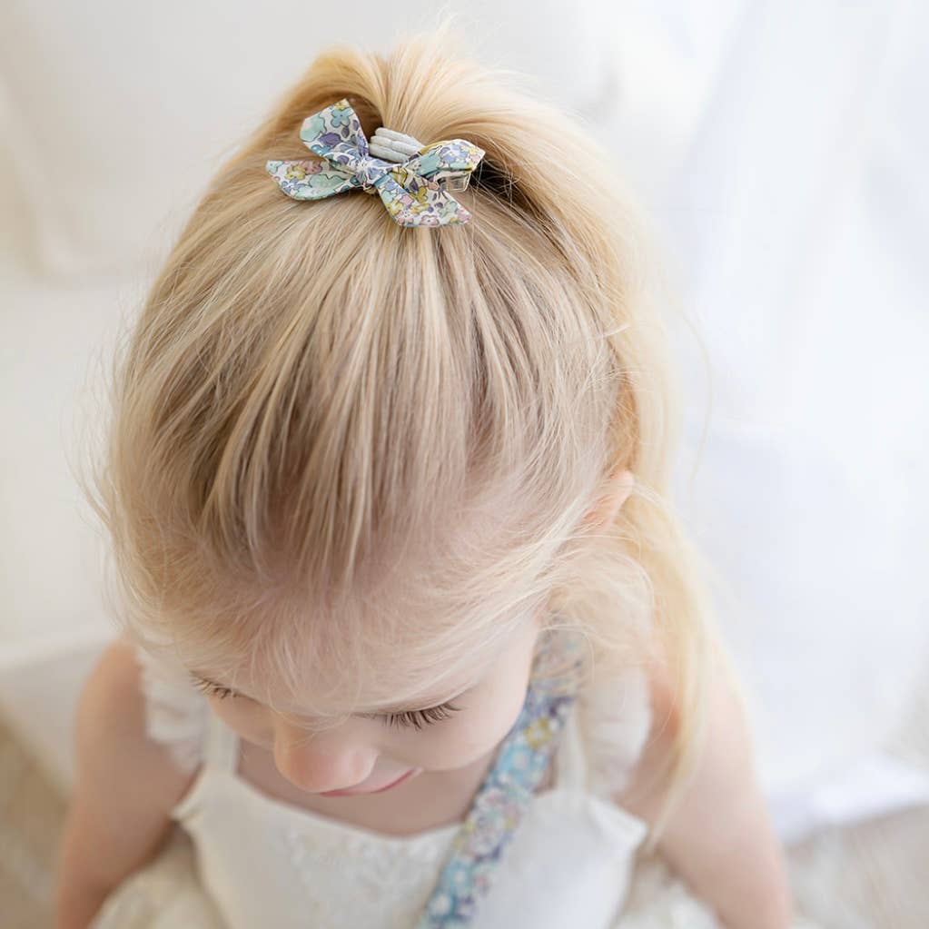 Child with blonde hair wearing a decorative bow hair clip against a neutral background