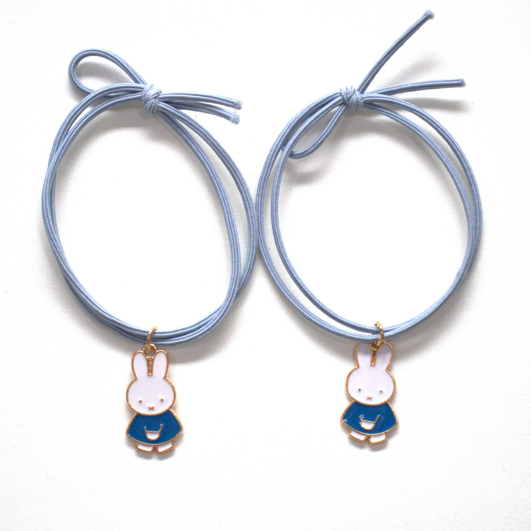 A pair of light blue elastics with small Miffy charms wearing blue dresses.