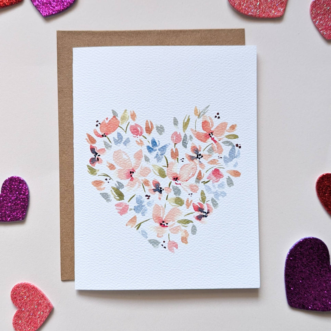 Card with floral heart design on a light blue background, surrounded by heart-shaped objects.