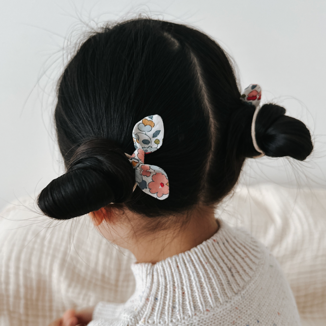 Child with black hair styled using floral hair elastic on a light background