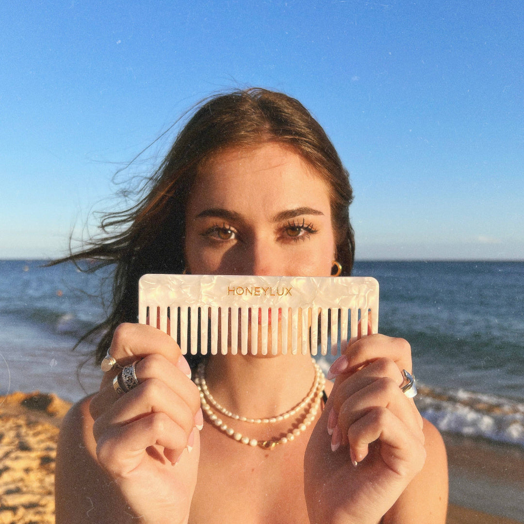 Woman holding a Honeylux comb in front of her face on a beach