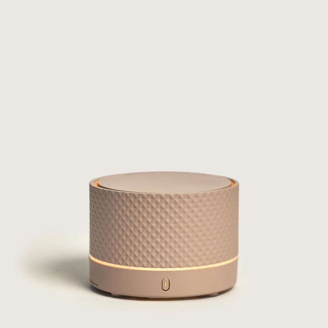 Round beige portable diffuser with textured surface on a light gray background