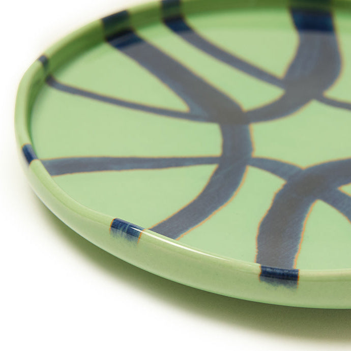 Close-up of a green ceramic plate with blue abstract patterns on a white background