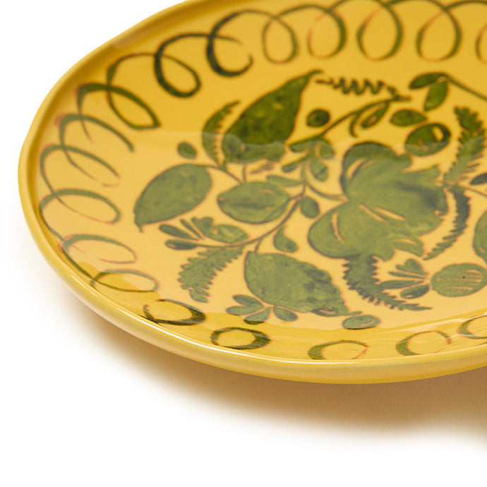 Yellow ceramic plate with green floral patterns on a white background