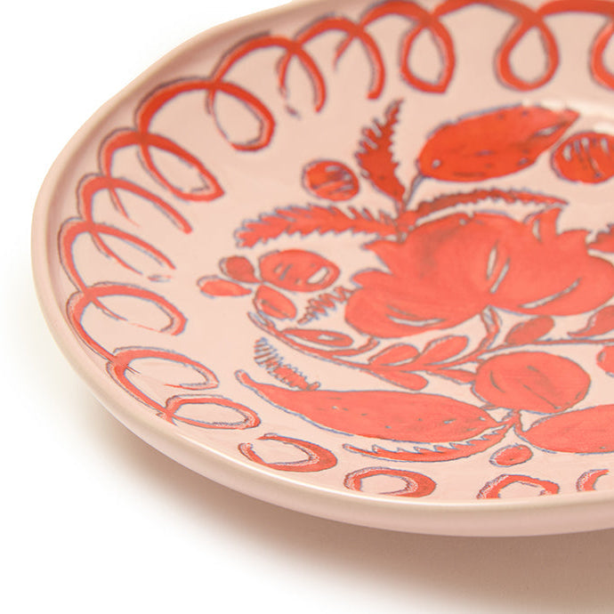 Pink decorative plate with floral design and red accents on a white background