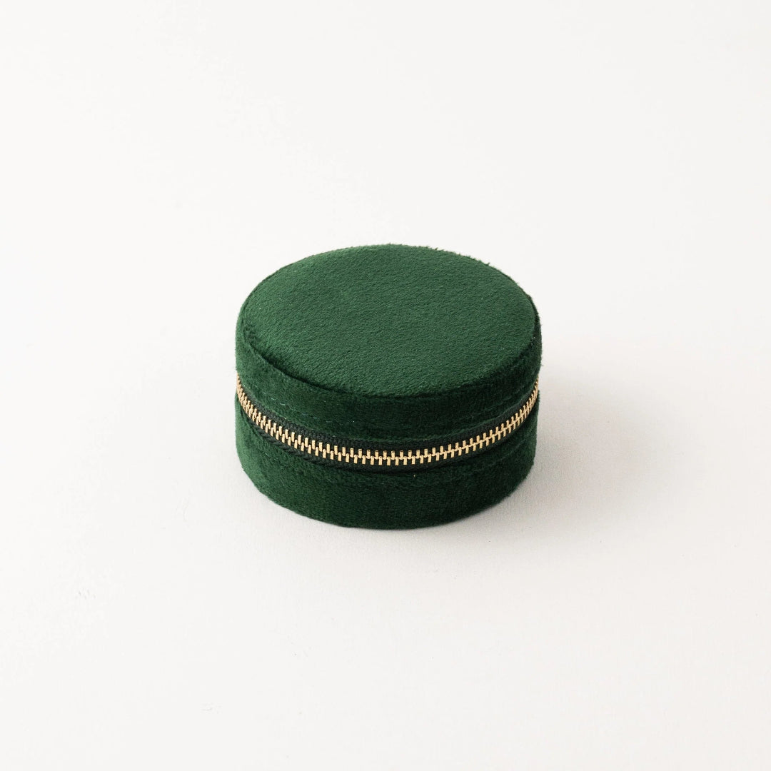 Green round jewelry box with a gold zipper on a white background