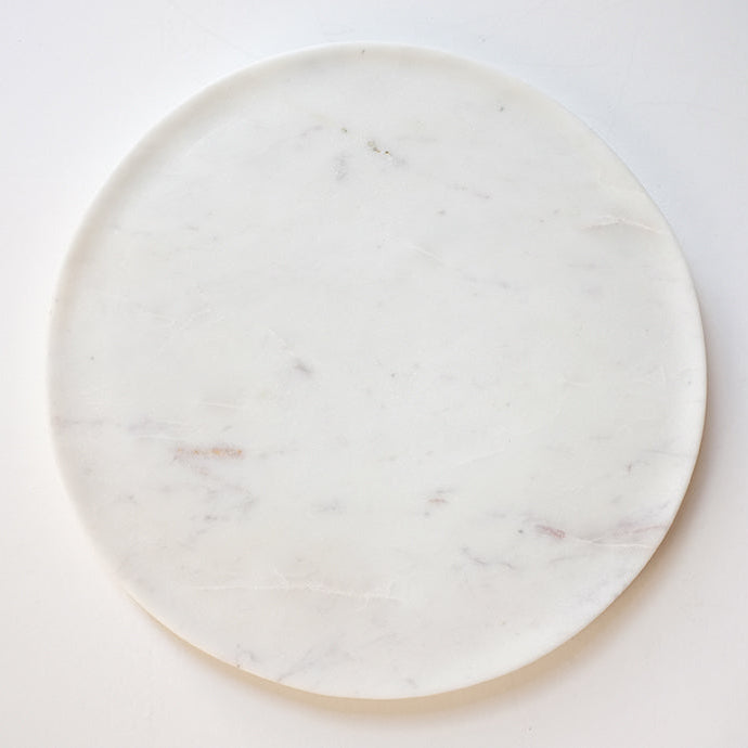 A round white marble cheese board with subtle swirling veins of gray and purple.