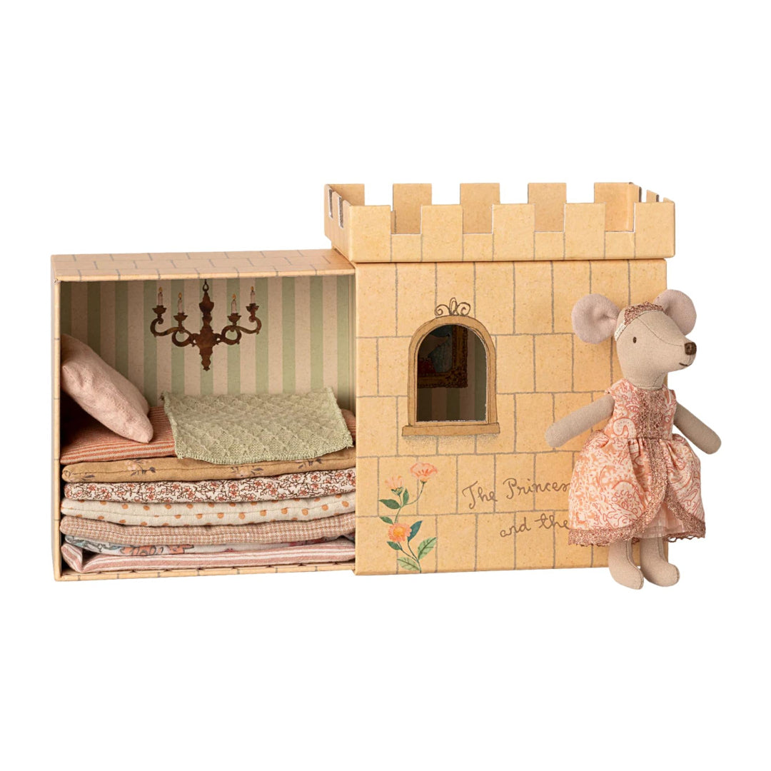 Cardboard castle toy with bedding and a mouse doll wearing a dress on a white background