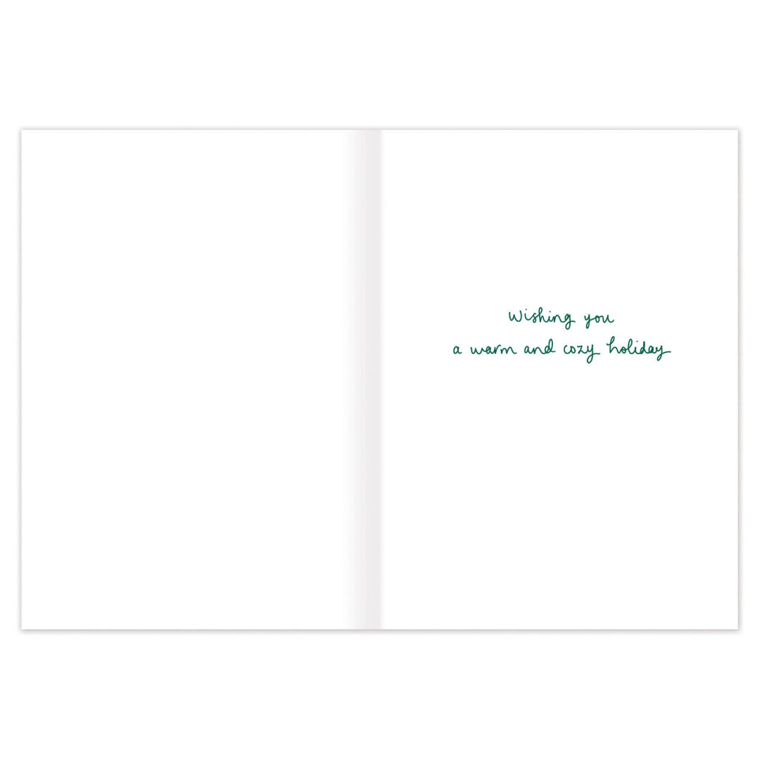 A blank greeting card shown open against a white background, with small green cursive text on the right side reading, 'Wishing you a warm and cozy holiday.'.
