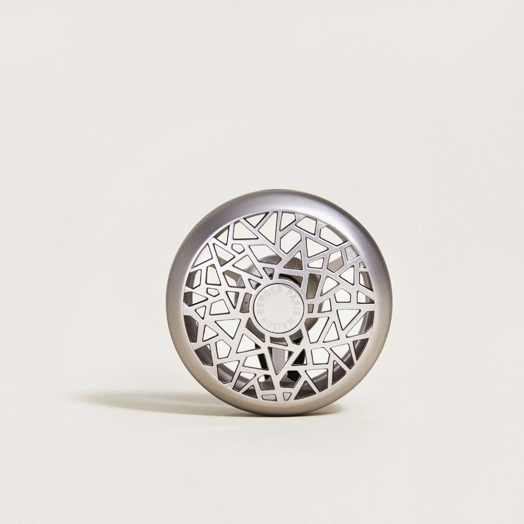 A round metallic silver car diffuser with an intricate geometric cutout pattern.
