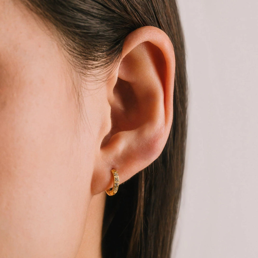 Close-up of an ear wearing a gold earring with a plain background