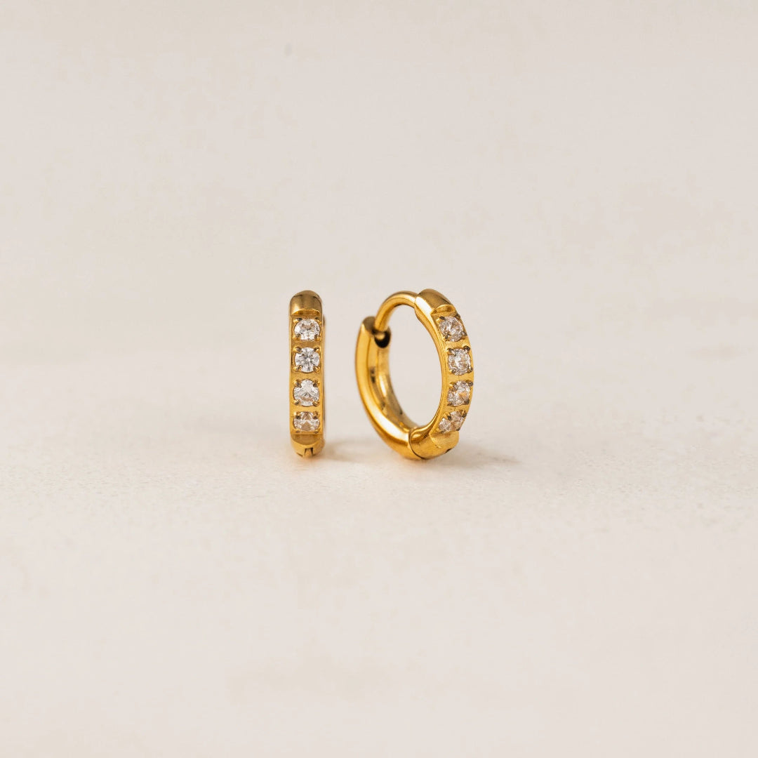 Gold hoop earrings with embedded stones on a beige background