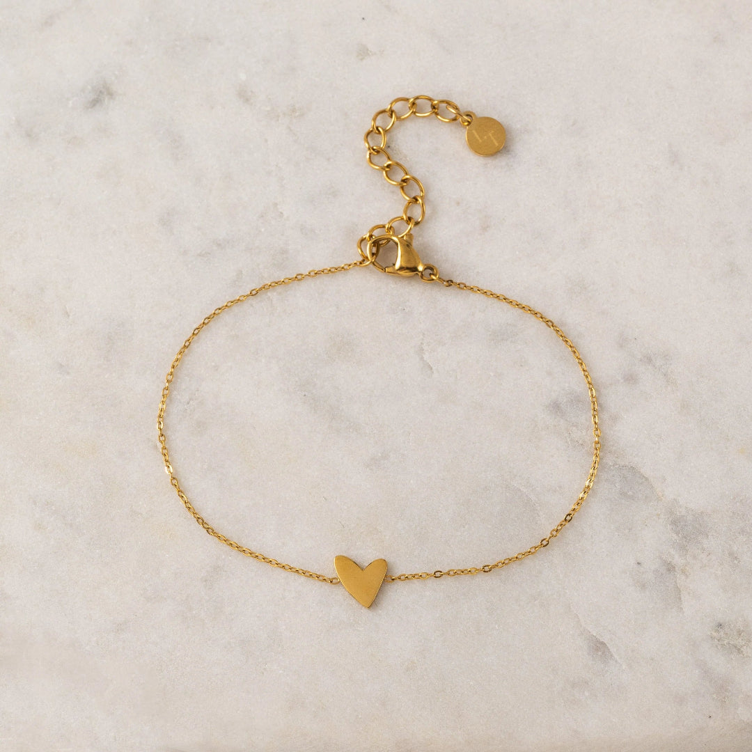 Gold bracelet with a heart charm on a marble surface